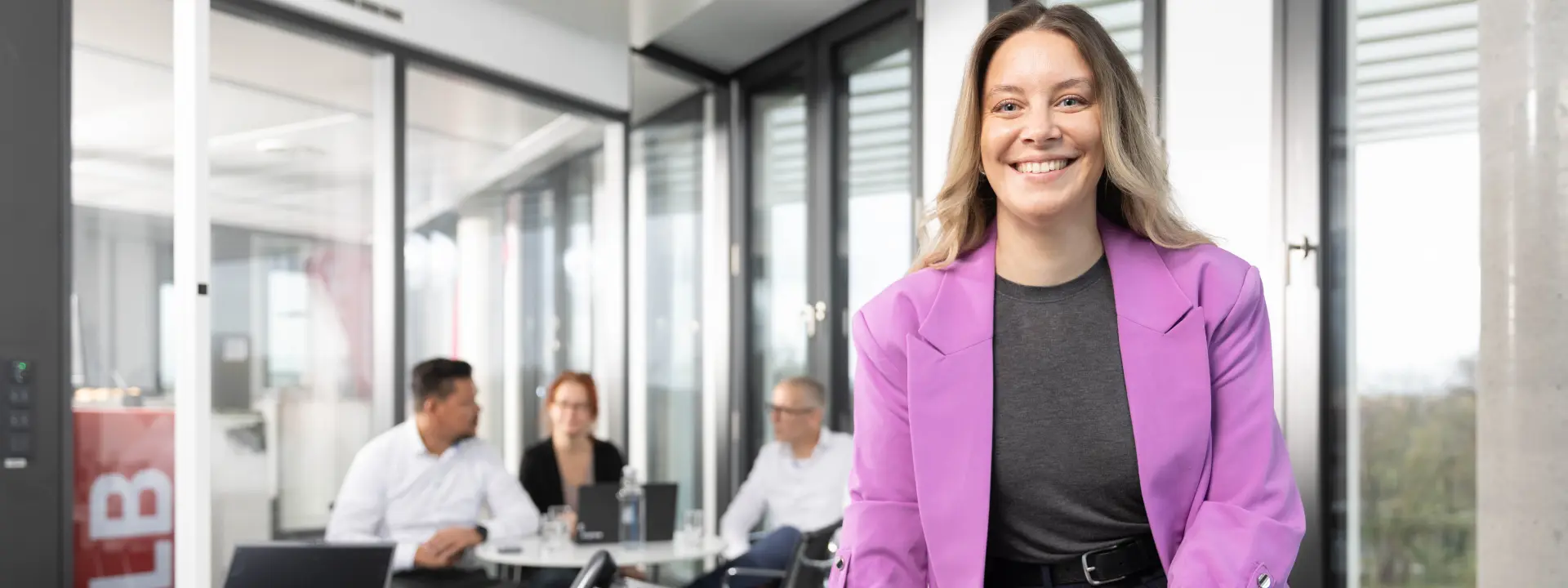 Drei junge Leute sitzen in einem modernen Raum mit großen Fenstern und weitem Blick über die Stadt vor ausgebreiteten Arbeitsblättern auf dem Boden.