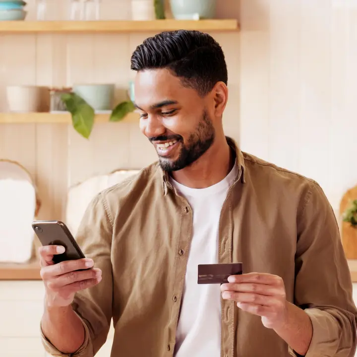 Mann hält Handy und Bankkarte in der Hand und ist freudig