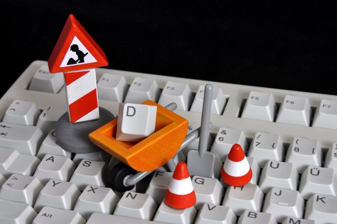 Wartungsarbeiten, sinnbildlich dargestellt an einer PC-Tastatur mit Mini Kegeln und Bauarbeiter Utensilien