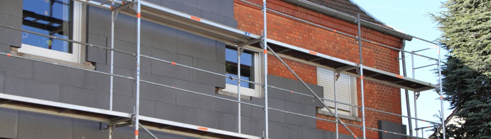 Eingerüstetete Fassade eines Hauses, an der zum Teil bereits Dämmung angebracht ist