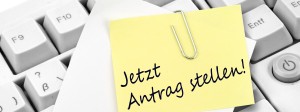Ein Zettel, auf dem: "Jetzt Antrag stellen!" steht, auf einer PC-Tastatur liegend.