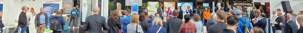Menschenmenge schaut in der Messehalle auf einbe Bühne und hört zu.